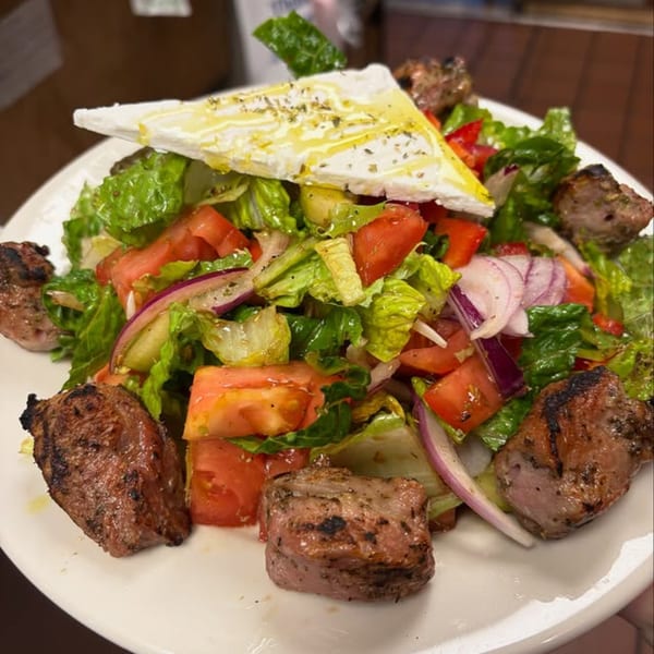 GRK Grill's Greek salad with grilled meat, lettuce, tomatoes, onions, and a large feta slice.