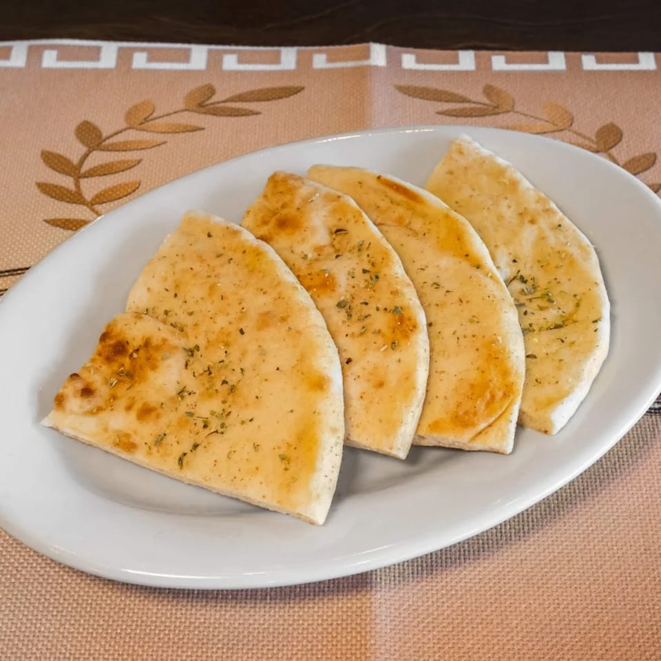 Four pieces of warm, seasoned pita bread on a white oval plate, ready to be served.