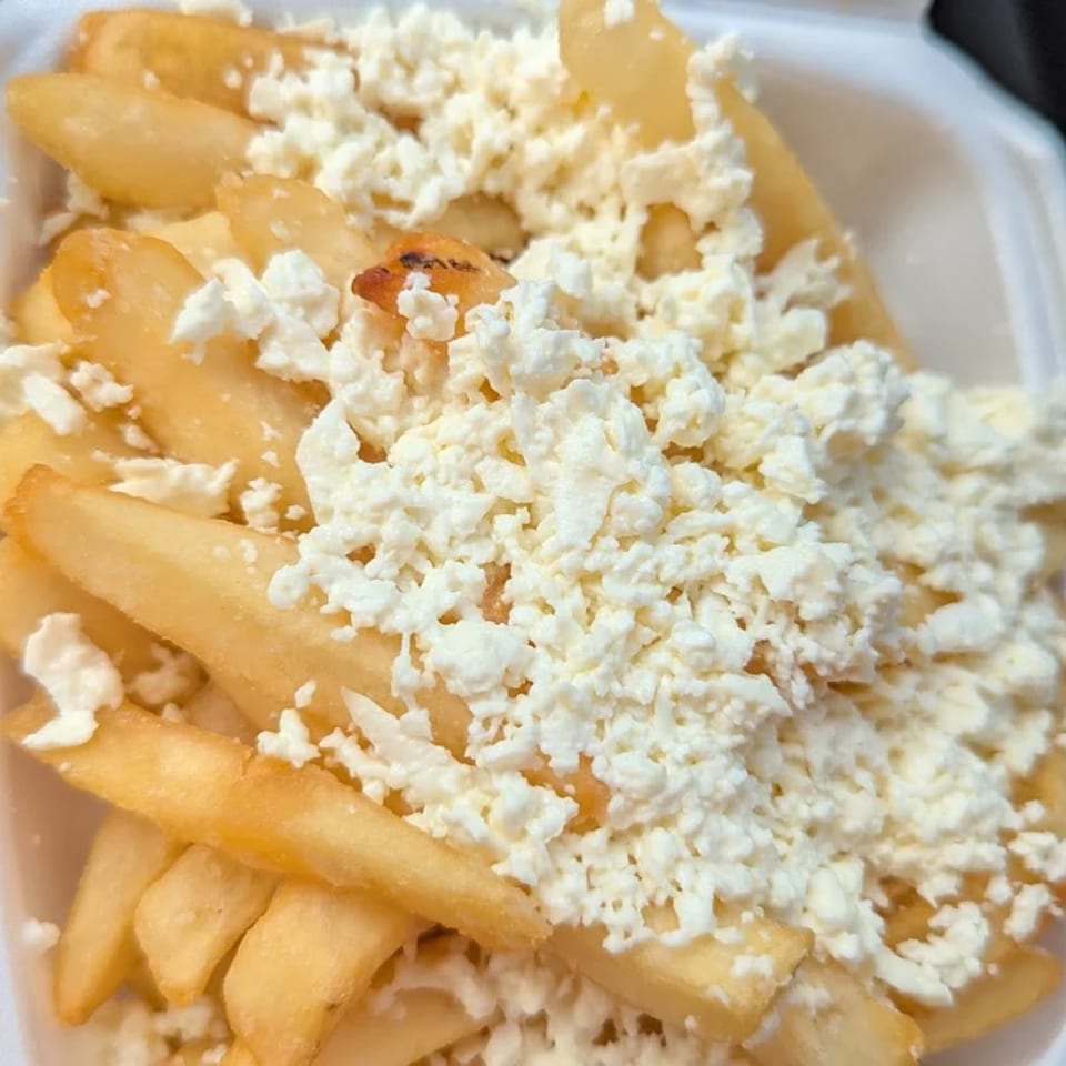 Golden french fries generously topped with crumbled white feta cheese, served in a white container.