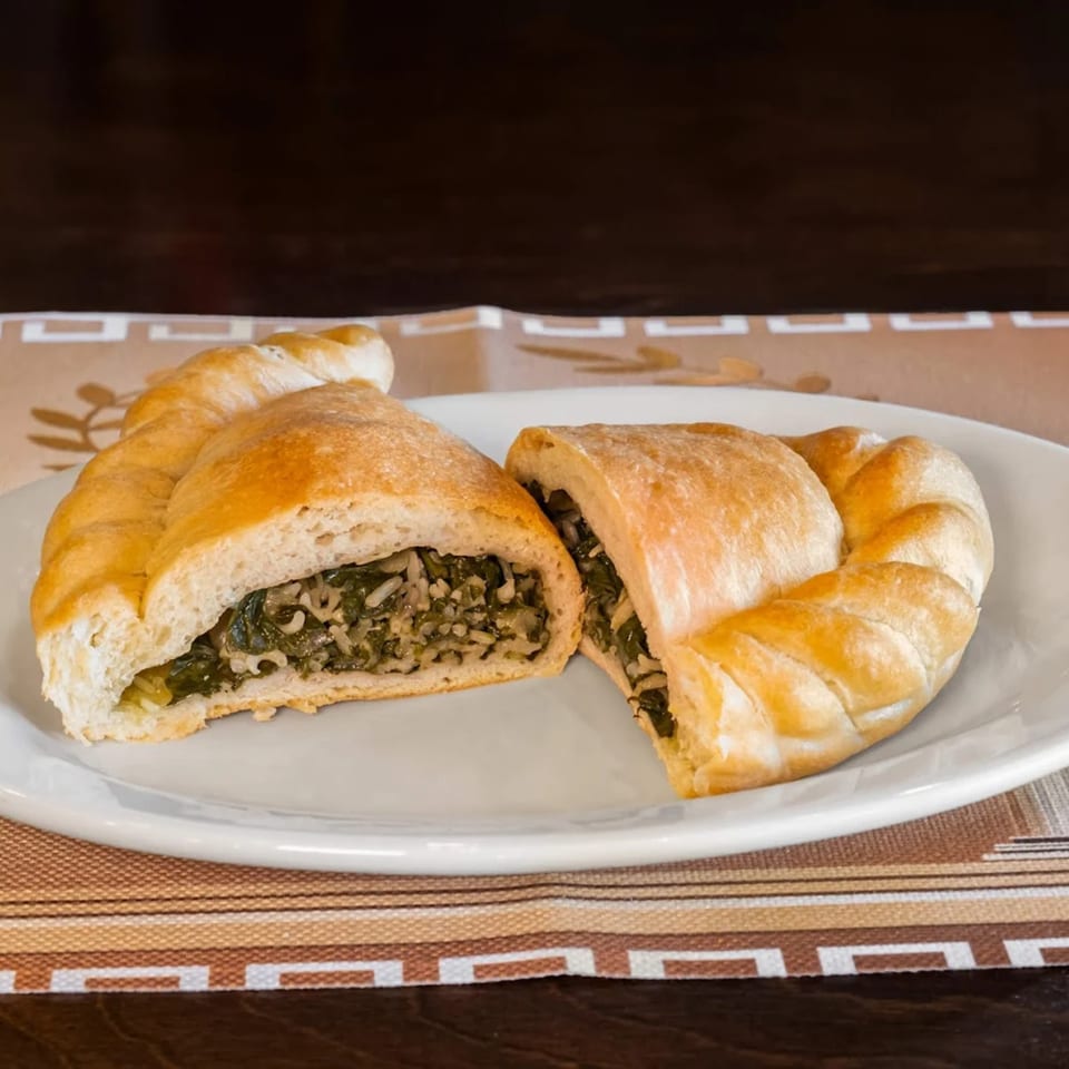 Two halves of a golden-brown Greek spanakopita, filled with spinach and rice, on a white plate.